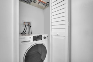 A compact laundry room with a front-loading washing machine, a dryer, and a power outlet with two cables. - Newly renovated 2BR Beachfront (Hollywood)