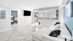 Een moderne woonkamer met een witte bank, een glazen salontafel en een wandgemonteerde flatscreen televisie.