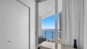 Une chambre avec vue sur la mer, un balcon avec une balustrade, un bureau avec une chaise et une fenêtre avec des rideaux.