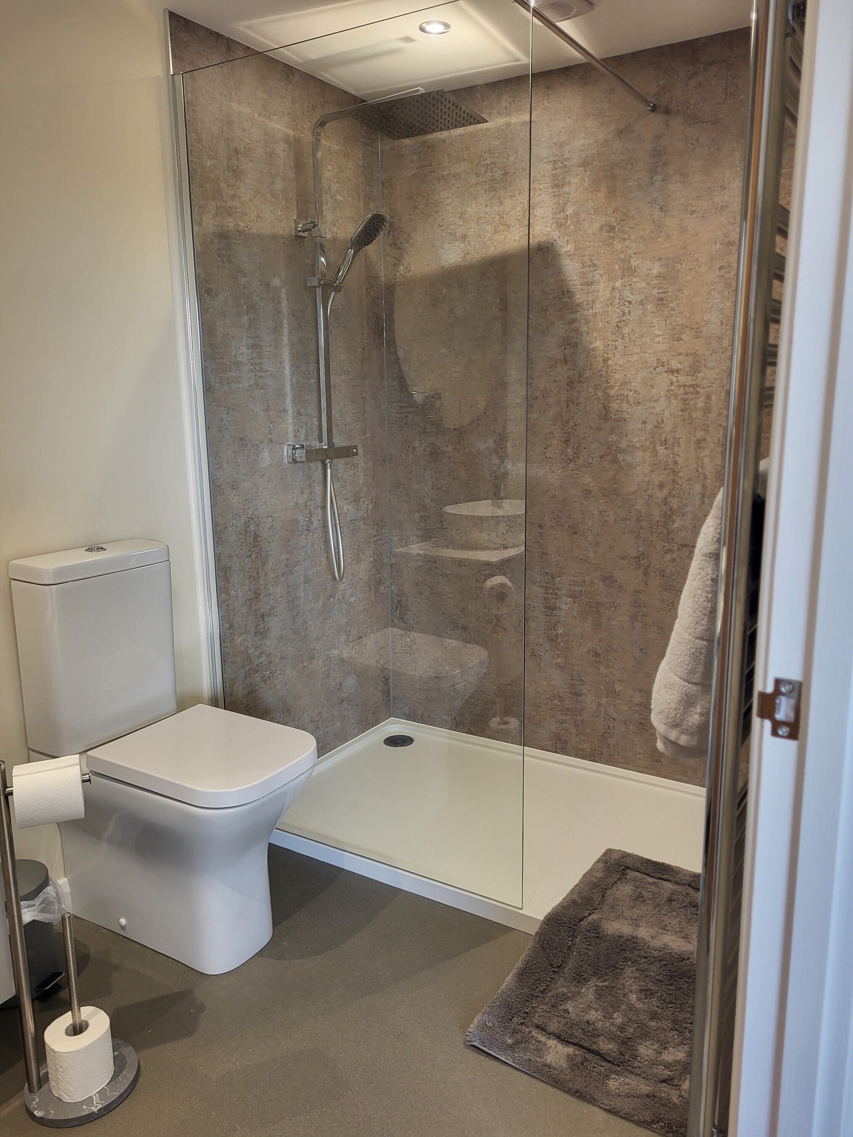 A modern bathroom with a glass-enclosed shower, a toilet, and a towel rack.