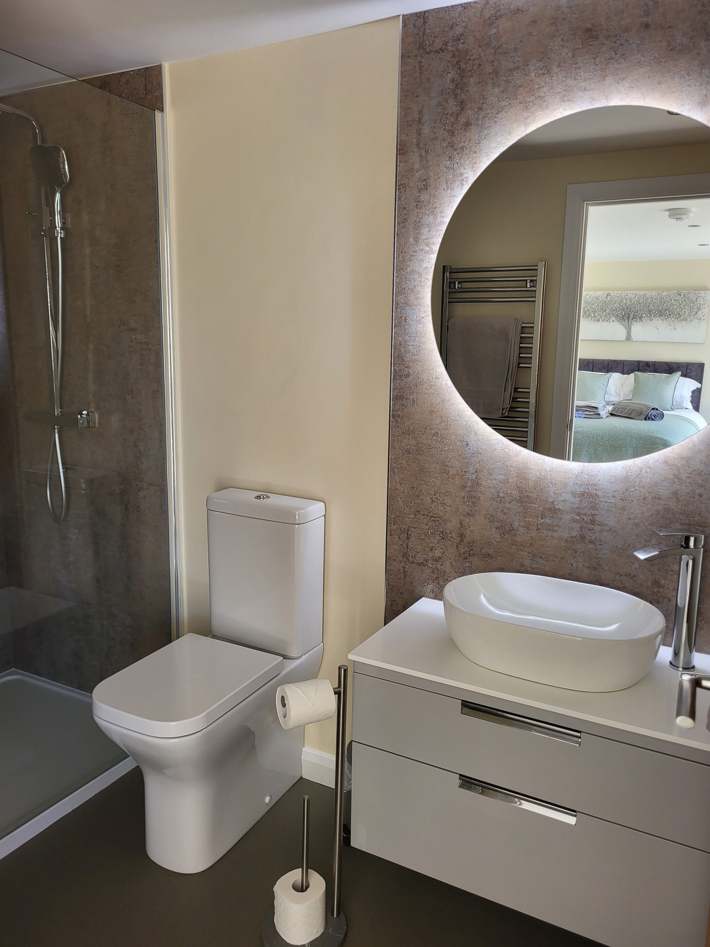 Une salle de bain moderne équipée d’une douche, de toilettes, d’un lavabo et d’un miroir à cadre rond.