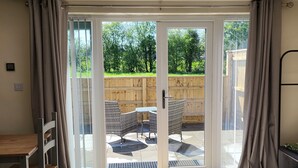 A room with a bed, a desk, and a view through a sliding glass door to an outdoor patio with a table and chairs. - The Old Barn (Redditch)