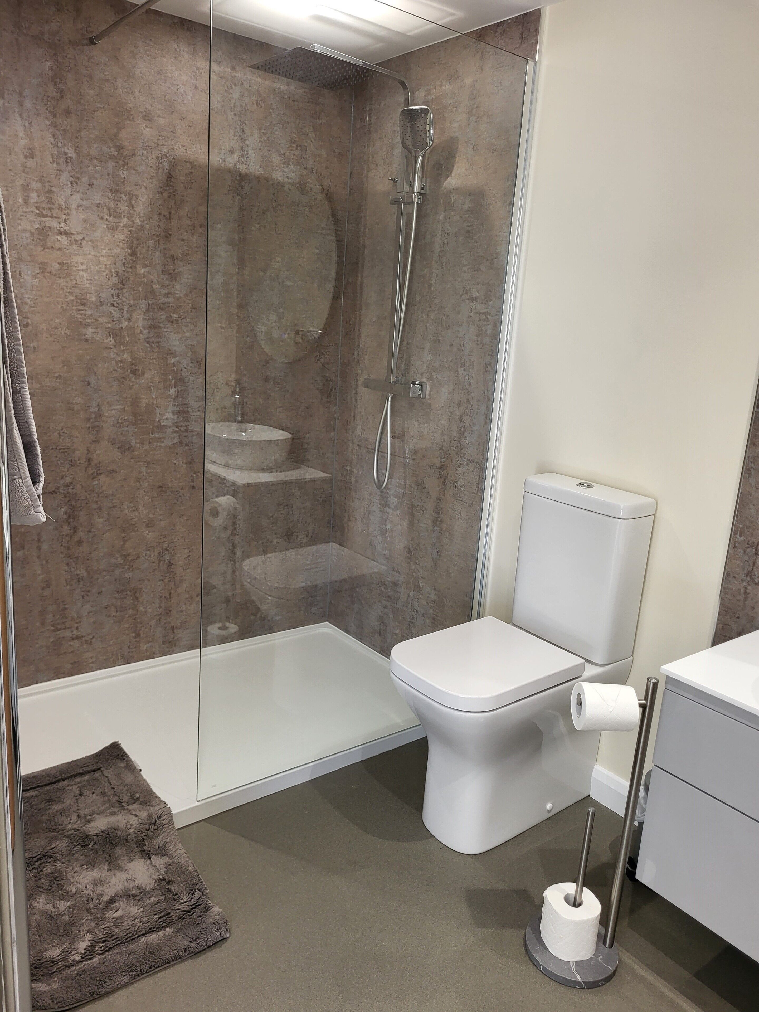 Un baño moderno con cabina de ducha de vidrio, inodoro blanco y suelo de mármol.