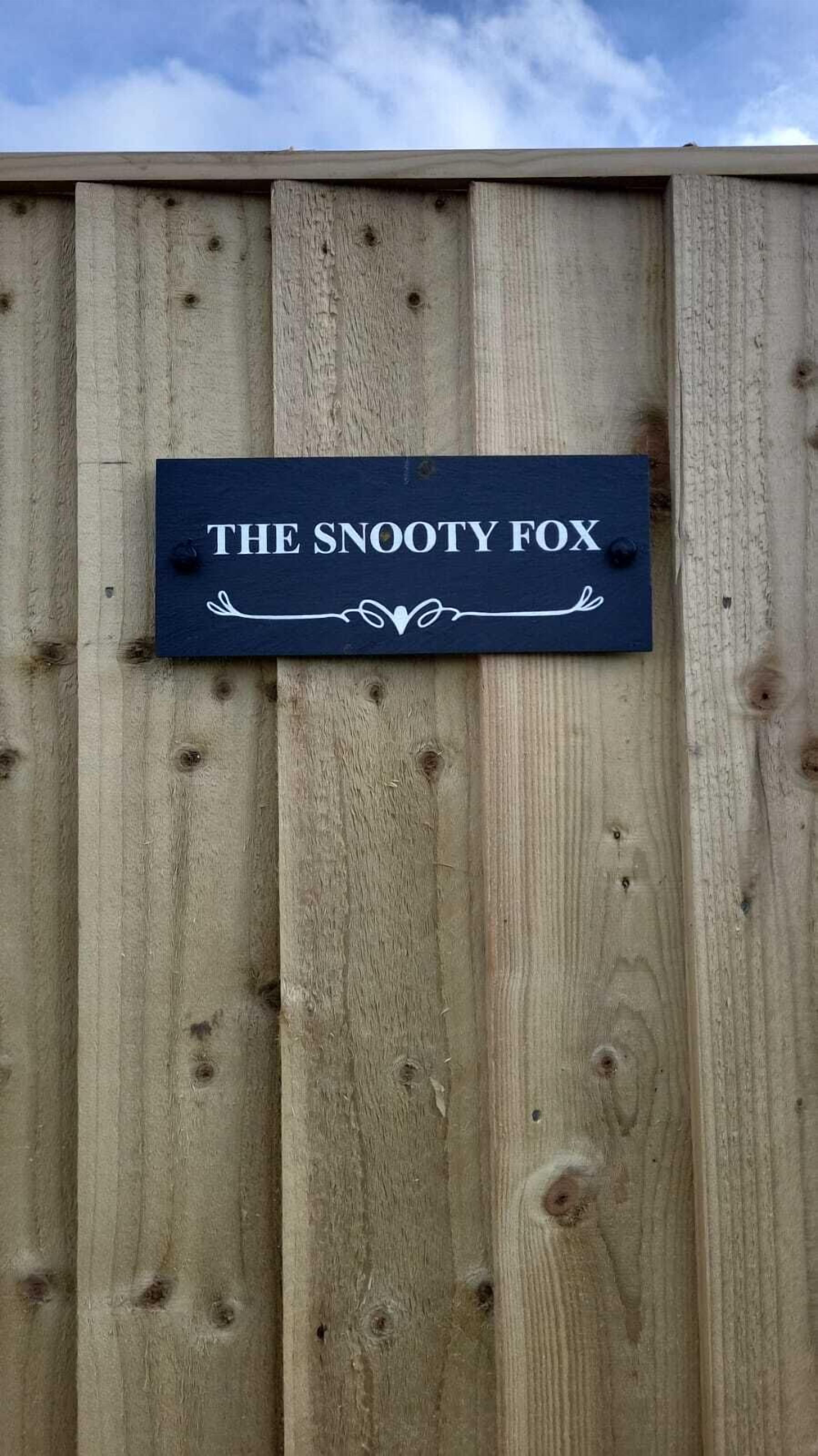Una valla de madera con un letrero que dice 'THE SNOOTY FOX'.