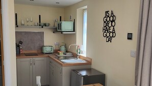 A compact kitchen with a wooden table and chairs, a microwave, and a toaster. - The Old Barn (Redditch)