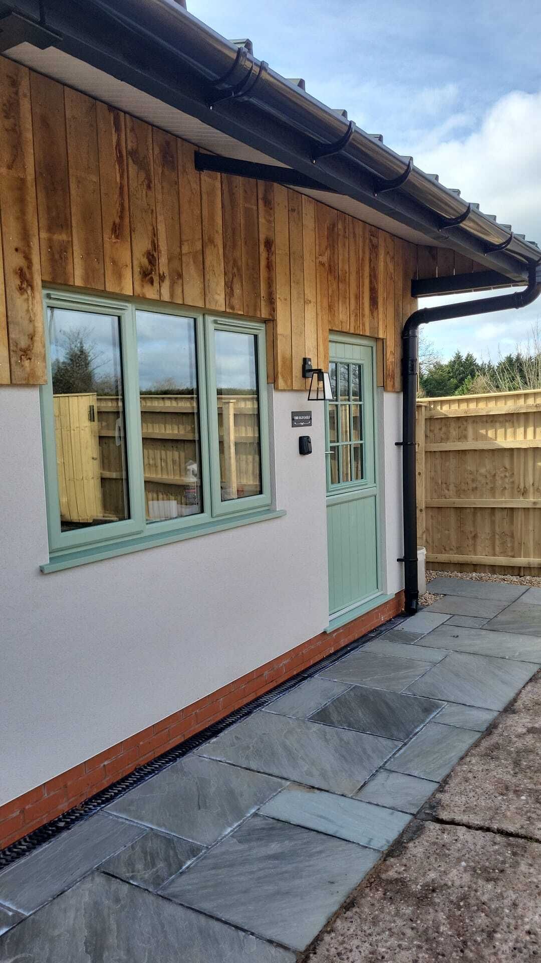 Ein Gebäude mit einer Holzfassade, einer grünen Tür und einem Fenster mit Blick auf einen Zaun und Bäume.