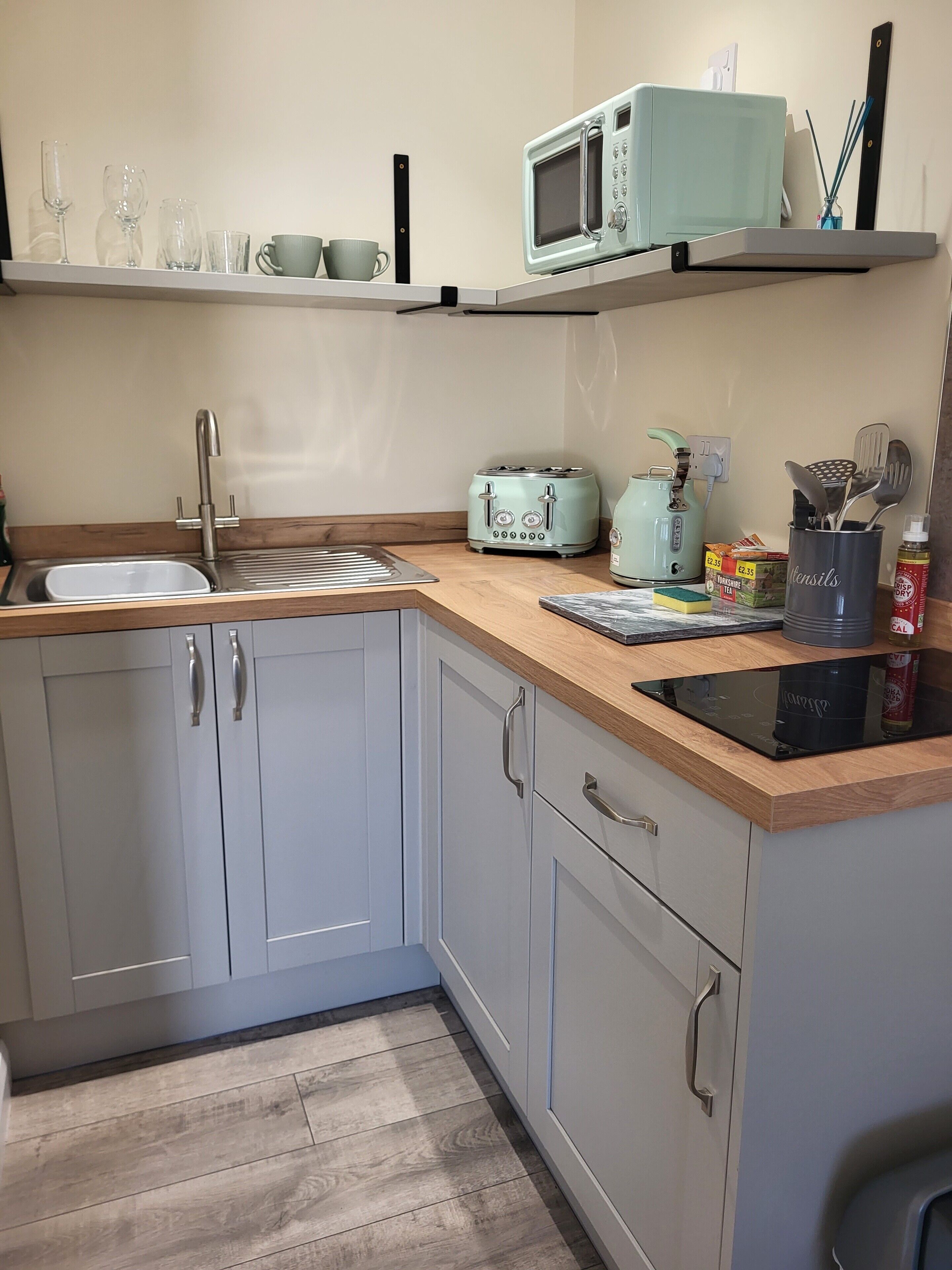 A kitchen with a sink, a microwave, a toaster, a kettle, and a spice rack.