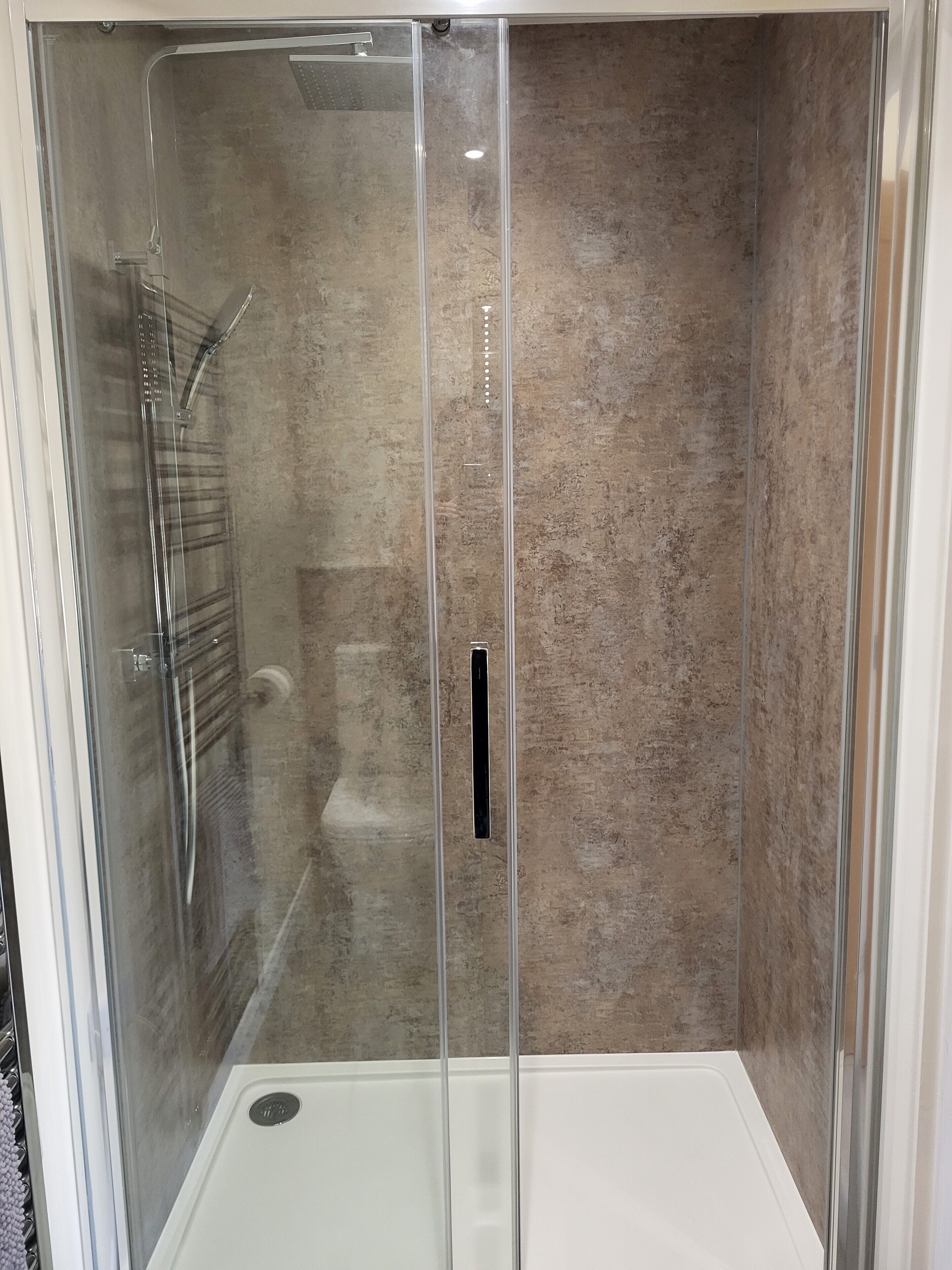 Un vestuario de ducha con paredes de vidrio, pared texturizada y suelo blanco.