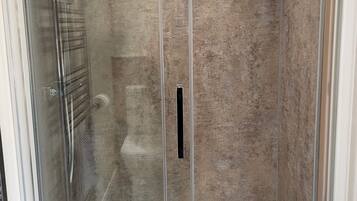 Un vestuario de ducha con paredes de vidrio, pared texturizada y suelo blanco.