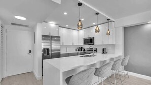 A modern kitchen with white cabinetry, a stainless steel refrigerator, a microwave, and pendant lighting. - Beautiful renovated 2BR unit ocean (Hollywood)