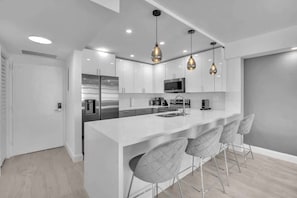 A modern kitchen with white cabinetry, a stainless steel refrigerator, a microwave, and pendant lighting. - Beautiful renovated 2BR unit ocean (Hollywood)