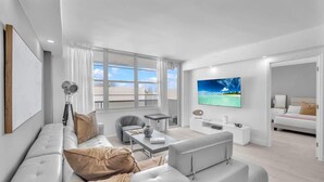 A modern living room with a sofa, a coffee table, and a TV. - Beautiful renovated 2BR unit ocean (Hollywood)