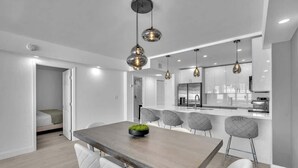 A modern kitchen with a central island, pendant lighting, and a dining area with a wooden table and white chairs. - Beautiful renovated 2BR unit ocean (Hollywood)