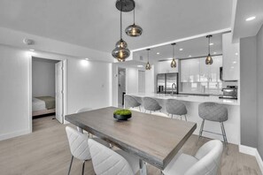 A modern kitchen with a central island, pendant lighting, and a dining area with a wooden table and white chairs. - Beautiful renovated 2BR unit ocean (Hollywood)