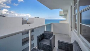 A balcony with a view of the sea, a glass railing, and wicker furniture. - Beautiful renovated 2BR unit ocean (Hollywood)