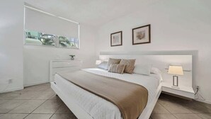 Une chambre à coucher moderne avec un grand lit, des tables de chevet, une fenêtre et des tableaux encadrés accrochés au mur.