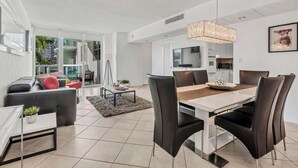 Un salon moderne avec un coin repas, de grandes fenêtres et une cuisine à l’arrière-plan.