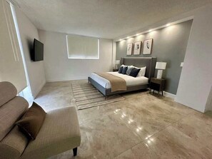 Ein Schlafzimmer mit Bett, Nachttischen, Fernseher und Fenster.