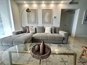 Ein modernes Wohnzimmer mit einer Eckcouch, einem Glastisch und zwei an Wänden befestigten abstrakten Kunstwerken.