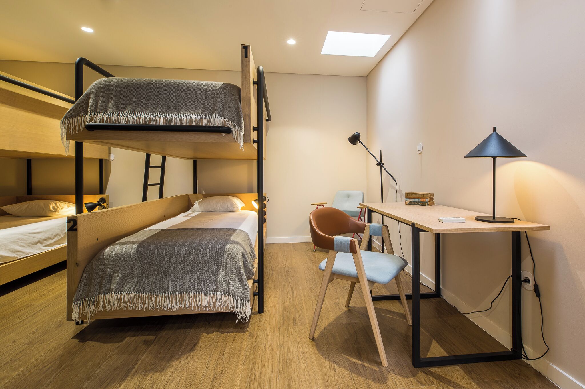Habitación con literas, escritorio, silla, lámpara y una pequeña mesa con libros.