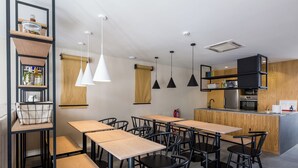 Une cuisine moderne dotée d’un îlot central, de tables en bois, de chaises noires, de luminaires suspendus et d’étagères intégrées.