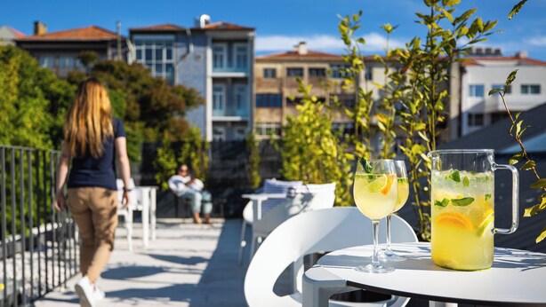 Une terrasse avec des sièges extérieurs, une table avec une carafe de thé glacé, et une personne qui marche au loin.