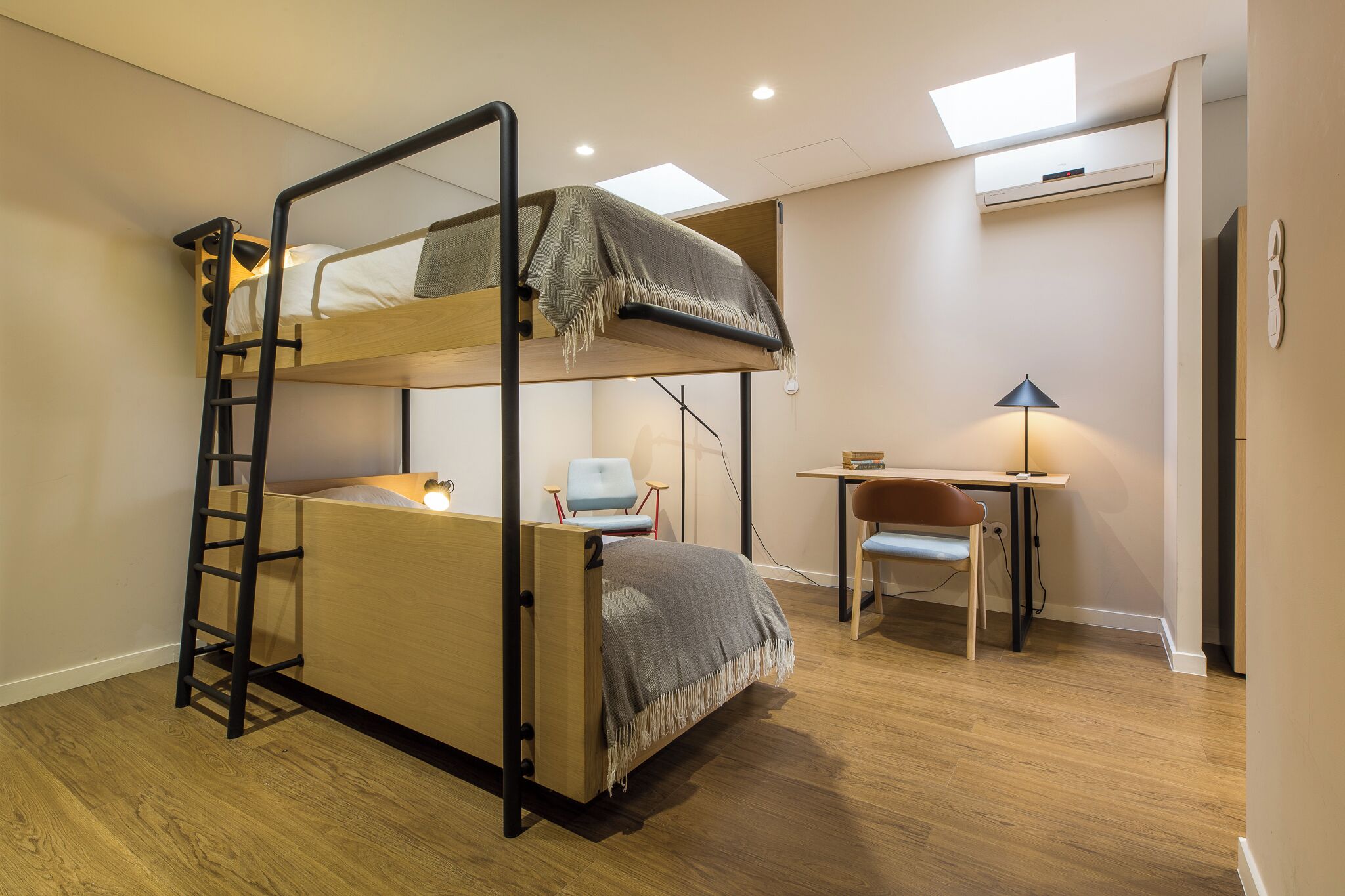 Uma cama beliche com uma escada, uma escrivaninha com uma cadeira e um abajur.