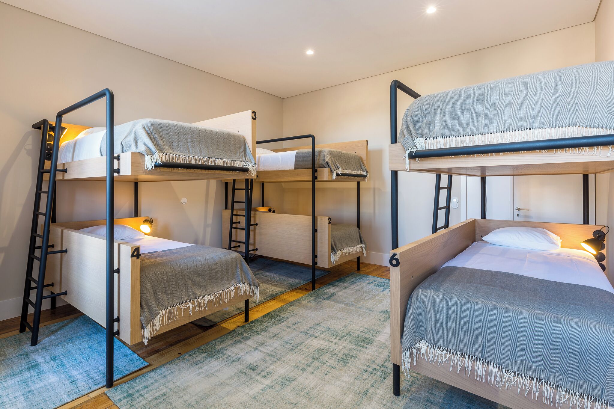 Une chambre de dortoir avec des lits superposés, chacun étant équipé d’une échelle, d’une petite table de chevet et d’une lampe.