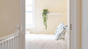Une chambre à coucher avec un lit, des murs blancs, une plante suspendue et une porte blanche.