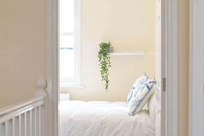 A bedroom with a bed, white walls, a hanging plant, and a white door. - Sandy Shores - Located in the heart of Filey (North Yorkshire)