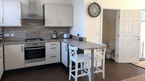 Une cuisine compacte avec des meubles blancs, un four encastré, une cuisinière à gaz et un plan de travail en bois.