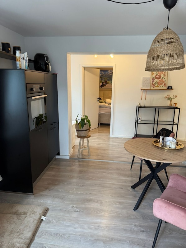Une cuisine moderne avec un réfrigérateur noir, une table à manger avec une chaise rose et un luminaire suspendu en osier.