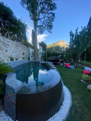 A swimming pool with a stone wall, a tree, and a mountain in the background. - Luna Rossa, Capri (Capri)