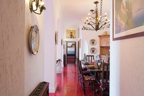 A hallway with a red-tiled floor, a dining area with wooden chairs and a table, and a chandelier. - Luna Rossa, Capri (Capri)