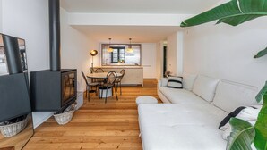 A modern living room with a sofa, a dining area with chairs, a kitchen with a stove, and large green plants. - Foz by the River (Porto)