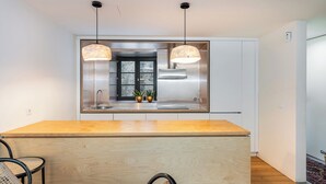 A modern kitchen with a central island, pendant lights, and a stainless steel range hood. - Foz by the River (Porto)