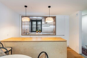 Une cuisine moderne dotée d’un îlot central, de luminaires suspendus et d’une hotte de cuisine en acier inoxydable.