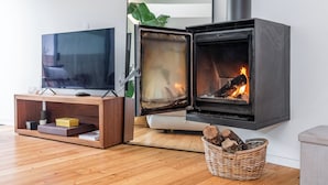 A modern living room with a television, a fireplace with visible logs, a wooden console table, and a wicker basket with logs. - Foz by the River (Porto)