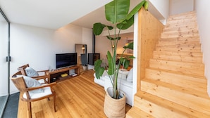 A modern living room with a wooden floor, a white sofa, a TV, and a large plant. - Foz by the River (Porto)