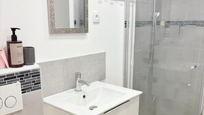 Un baño con lavamanos blanco, espejo, cabina de ducha y retrete.