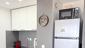 Una cocina compacta con armarios blancos, microondas integrado, refrigerador, lavamanos y un bote de basura.