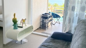 Una sala de estar con un sofá, un televisor de pantalla plana, una mesita con figuritas y vista al mar a través de un ventanal corredera.