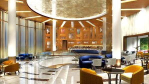 Een ruime lobby met een gebogen glazen balustrade, blauwe banken, gele stoelen en een centraal zitgedeelte met tafels.