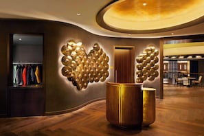 A modern lobby with a wooden floor, a large gold decorative wall, and a clothing rack.