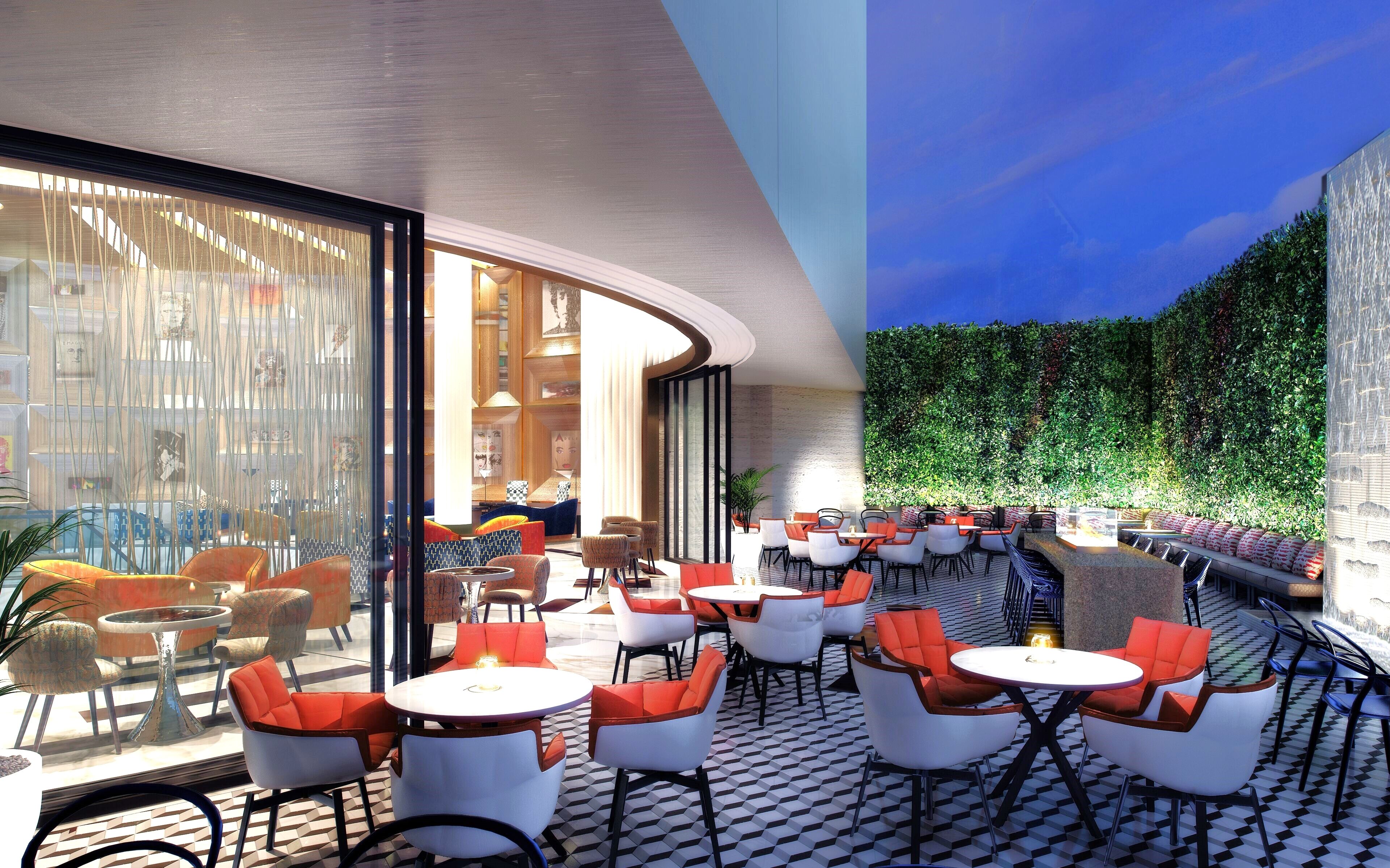 A modern outdoor seating area with round tables and chairs, large windows, and a green wall.