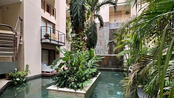 Un atrium à plusieurs niveaux, doté d’un élément aquatique central, entouré d’une végétation luxuriante et présentant un design architectural moderne.