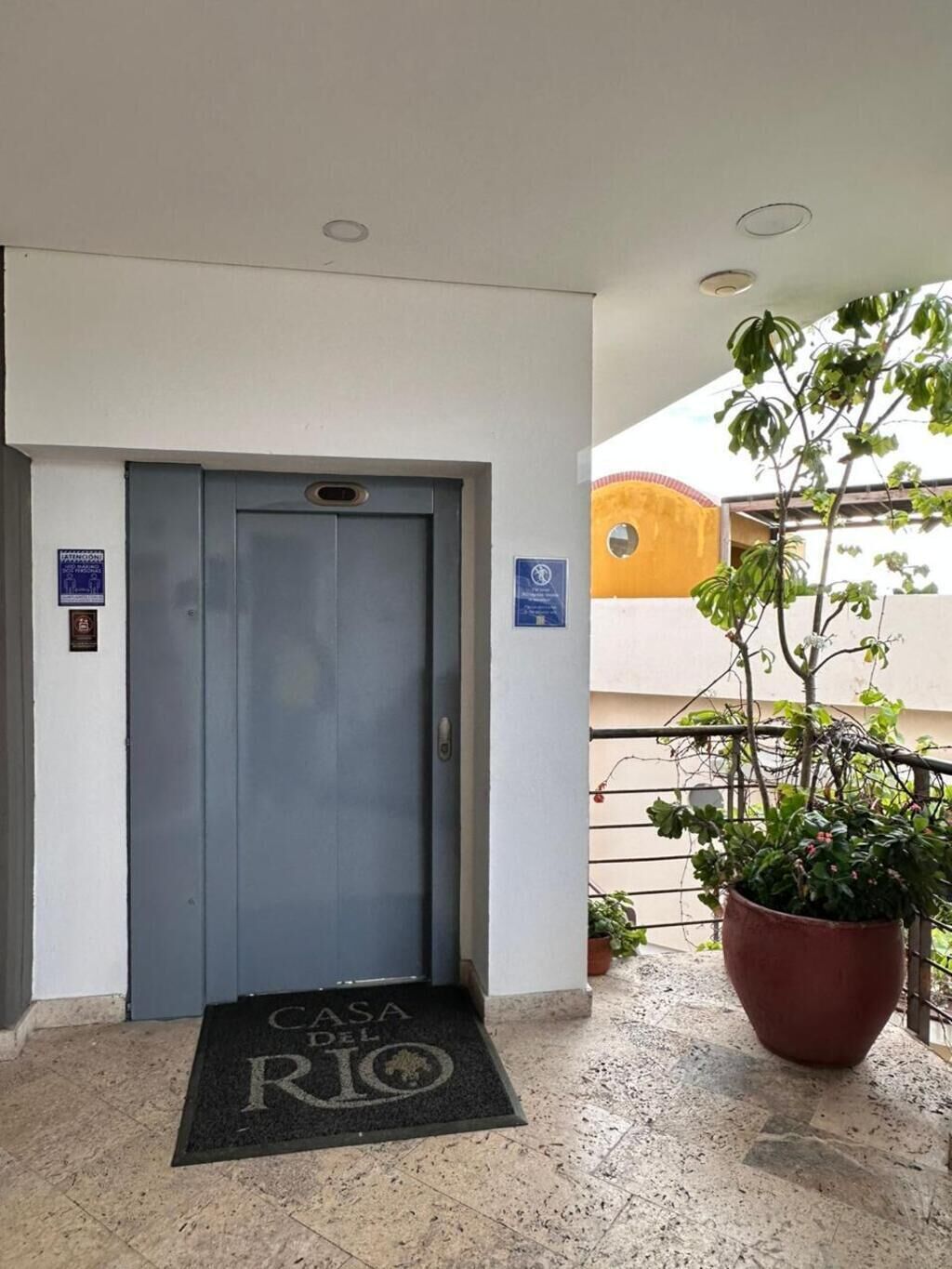 Een hotelentree met een grijze deur, een deurmat en een bloempot aan de rechterkant.