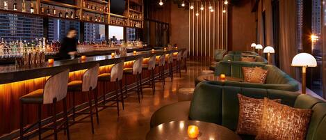 A bar area with a long counter, multiple stools, and a seating area with couches and tables.