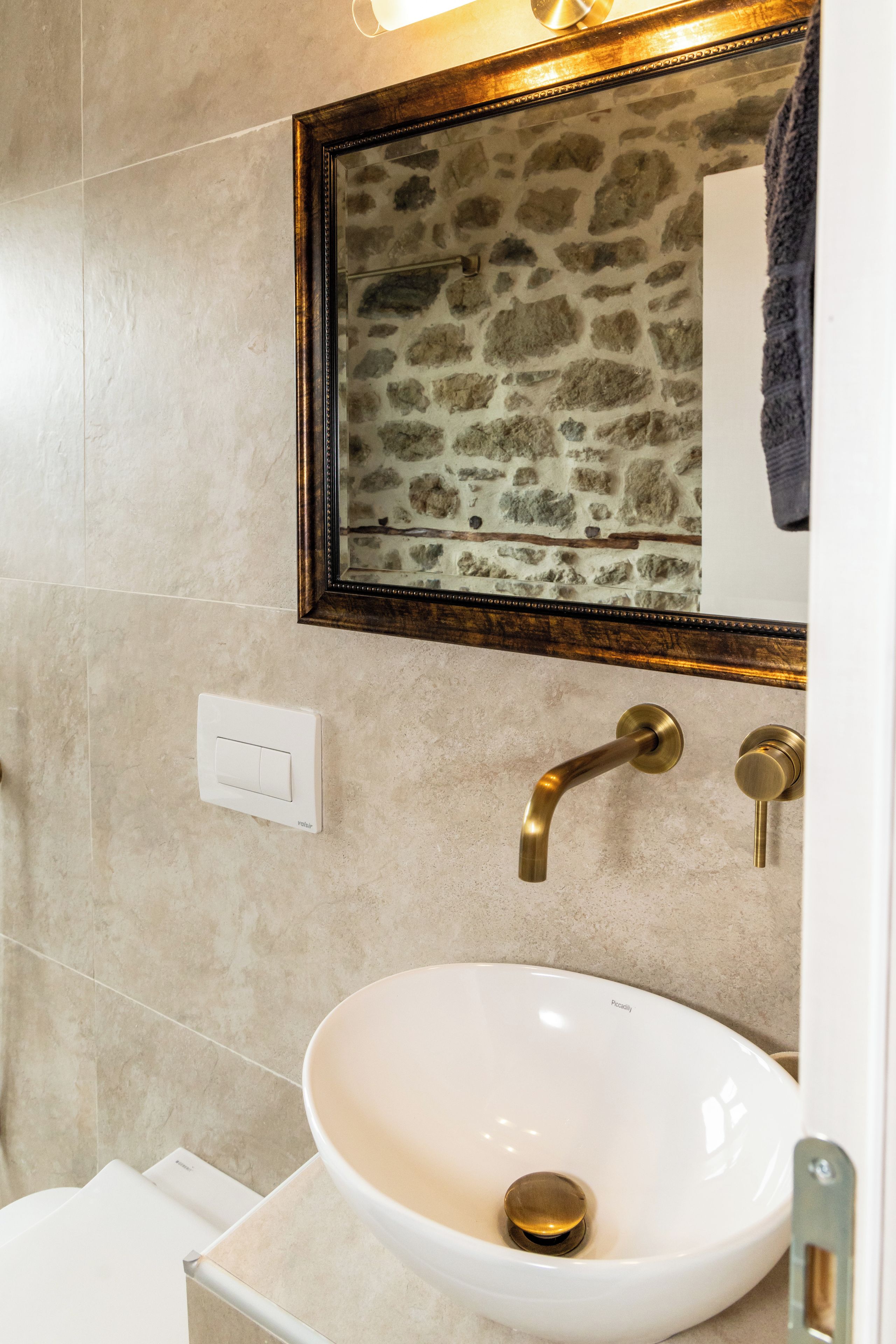 A bathroom with a stone wall, a white sink, and a mirror with a wooden frame.