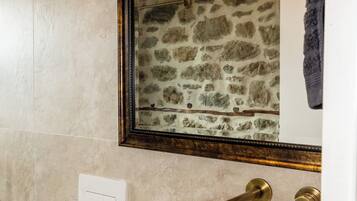 A bathroom with a stone wall, a white sink, and a mirror with a wooden frame.